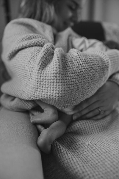 motherhood sessions with newborn baby and mom. black and white photo with tiny baby feet in newborn nursery at home.