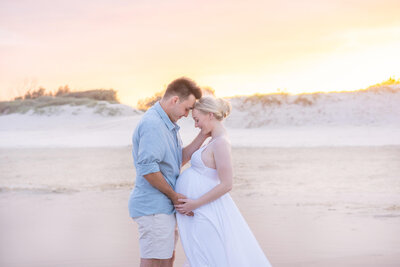 couple posing for maternity photos on the beach with pastel sunset in Gold Coast