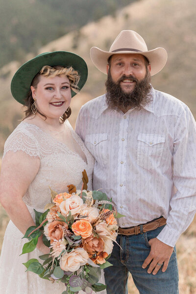 A bride in an detailed lace gown and her groom stand holding hands, noses together outside of their venue just after their Colorado elopement