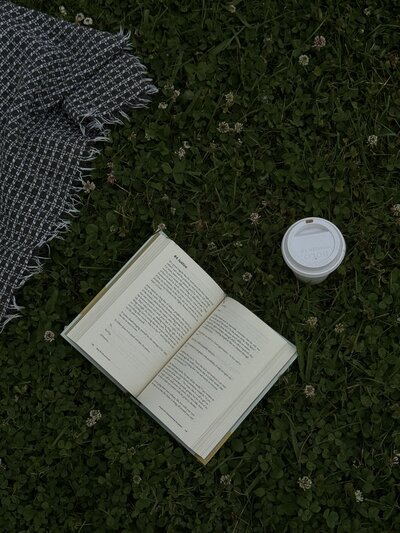 An open book and a to-go coffee cup laying on the grass