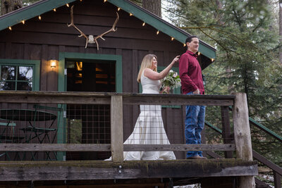 Bride touching grooms shoulder for first look on porch of rustic cabin in the woods.