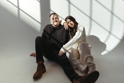 couple sitting on floor leaning on each other in front of white backdrop