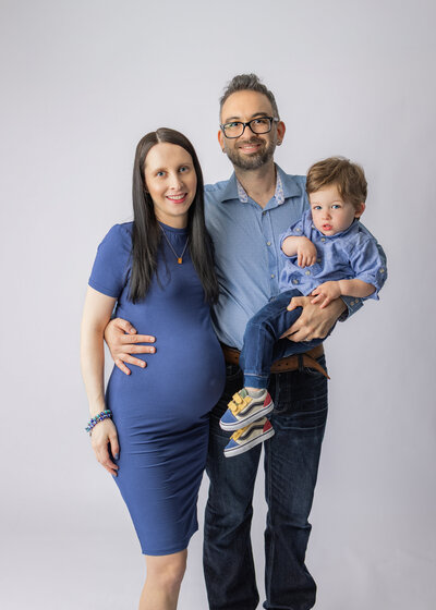 Pregnant mother with partner and toddler son smiling together during studio family maternity photoshoot in NJ