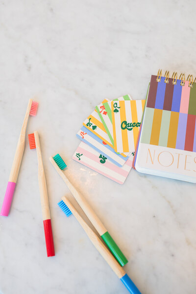 Flatlay of colorful wooden toothbrushes, a striped notebook, and colored striped playing cards