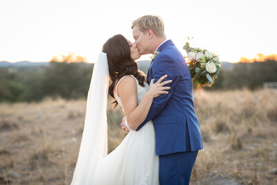 An Austin-based wedding photographer captures a bride and groom passionately kissing in a field at sunset.
