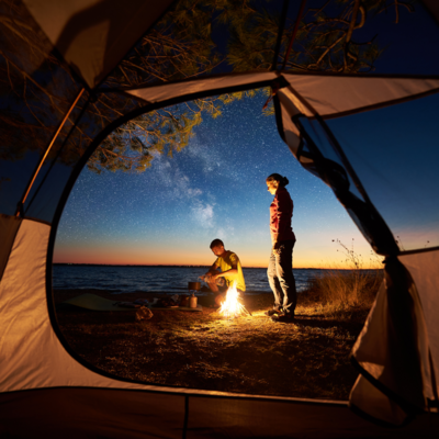 people standing in front of open tent stoking a campfire.