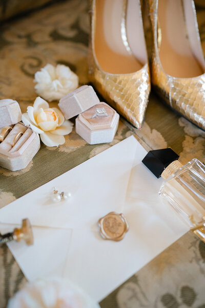 luxury destination wedding flat lay of gold bridal shoes, wedding ring, perfume and the timeline. 