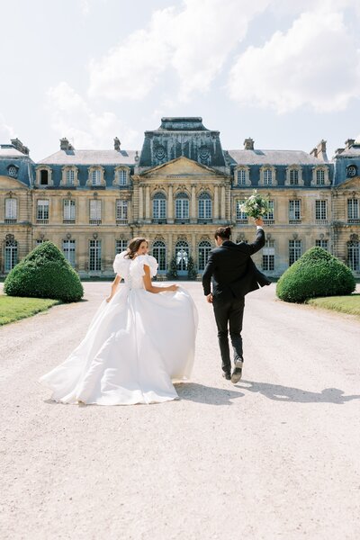 Bride and groom running towards the Château de Champlâtreux