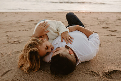 couple laying in sand for san clemente engagement session