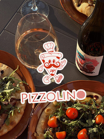 Maquette de présentation de l'identité visuelle de Pizzolino, qui représente une ambiance gourmande et traditionnelle. L'image montre une table garnie de plats avec le logo vertical de la marque.