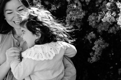 A black and white photograph showing joyful laughter and embrace outdoors with cherry blossoms in the background.