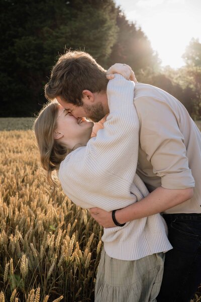 A woman holds her fiance close and leans in to kiss him as they stand in a wild flower patch in an Aberdeen park during their engagement session.