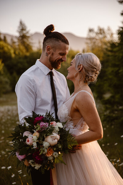 couple in wedding attire with bouquet embraces in front of Olympic Mountain range