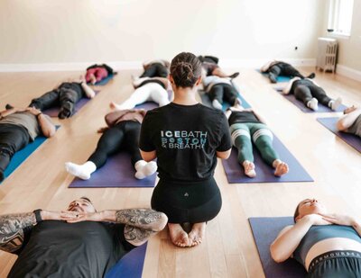 A breathwork coach seated on a yoga mat, guiding participants through mindful breathing techniques in a calming studio environment.”