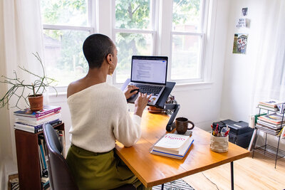 Michaela Ayers sitting at her desk and typing on her laptop, planning a coaching session for her clients virtually