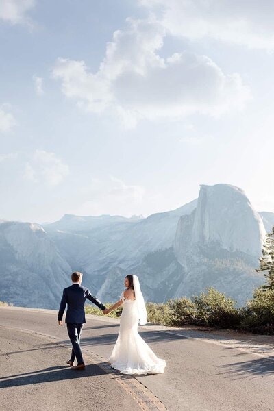 A bride and groom hold lanterns at dusk, while looking at the back side of Half Dome in Yosemite National Park. 
