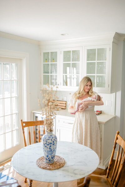 Newborn session photo in the client's home nursery, where mom sits in a rocker holding the baby, while dad kneels beside them, lovingly looking at their newborn. The warm, cozy nursery setting adds to the intimate family moment