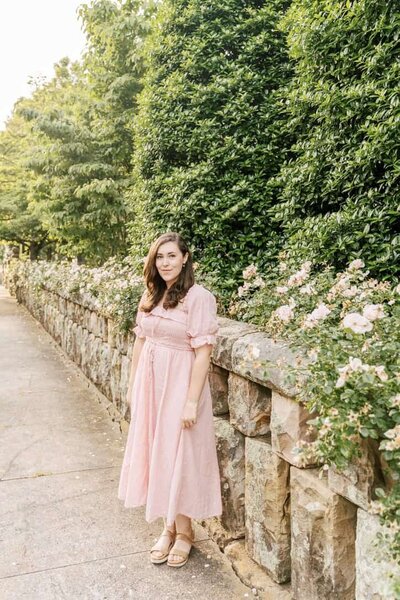 headshot of lookout mountain photographer kelley hoagland standing in front of old stone fence covered in roses