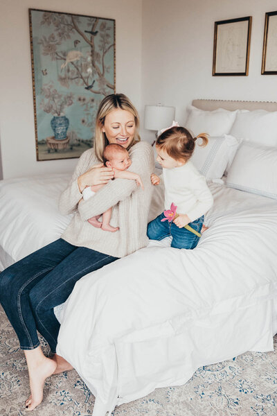 a mom holds her newborn baby while big sister admires her in their home in Del Mar