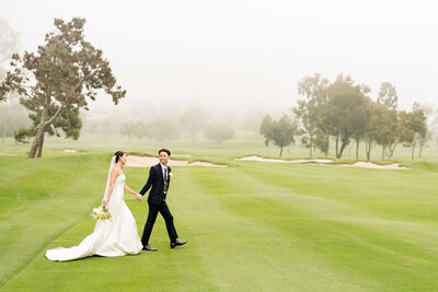 Bride and groom holding hands and walking with the sunset in the background on their wedding day at The La Jolla Country Club wedding venue