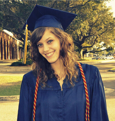 Girl wearing blue graduation cap and gown smiles at camera.