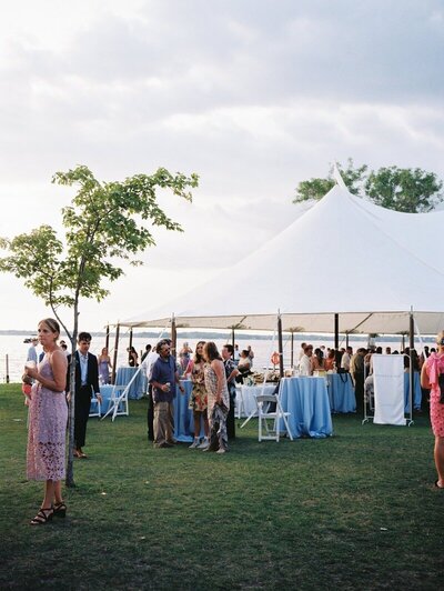 guests outside at outdoor wedding event under a white tent with trees and sky in the background by minnesota wedding photographers tom thornton photography