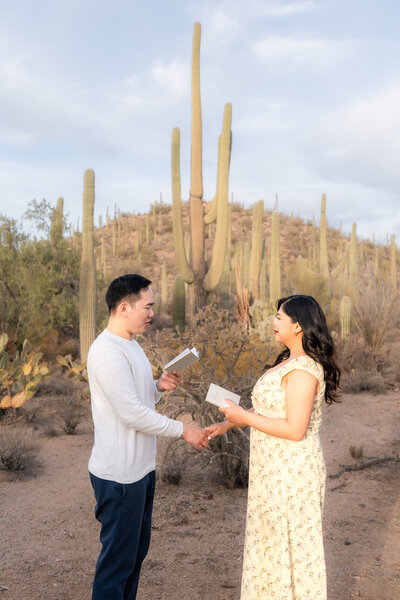 Asian couple bride and groom eloping at Saguaro National Park Arizona exchanging vows during sunset elopement ceremony at Valley View Overlook trail.