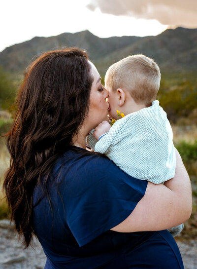 Mother kissing young son on cheek for comfort. Captured by Cactus & Pine Photography in Arizona