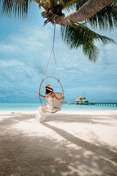 Woman on a beach swing facing the ocean