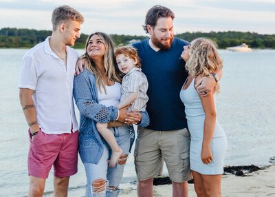a family on the beach with two teenage children and a younger child all looking lovingly at each other