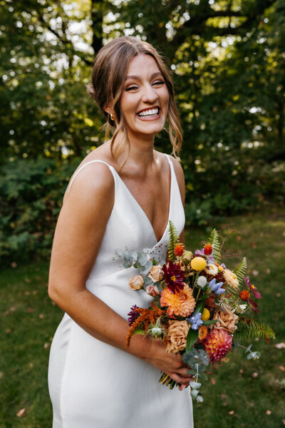 Blonde bride in a strapless white dress and brunette groom in a blue suit smile at their minneapolis wedding photographer while holding a margarita and old fashioned cocktail