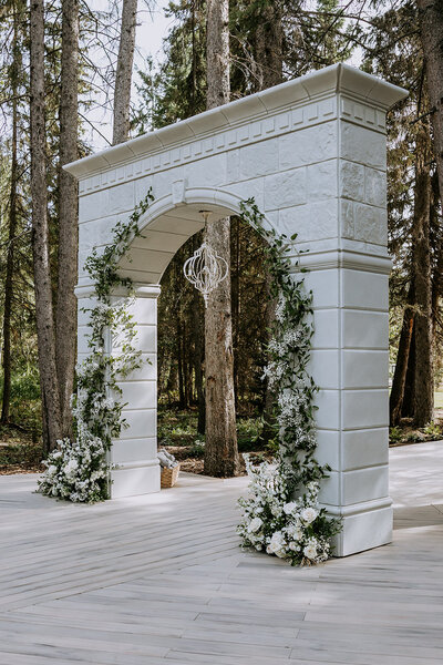 Ceremony arch decorated with florals, tucked amongst tall spruce trees