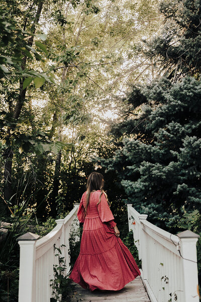 Patty walking away from the camera in a pink dress crossing over a white bridge 