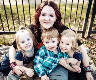 a teenage girl holds her three younger cousins while they all smile