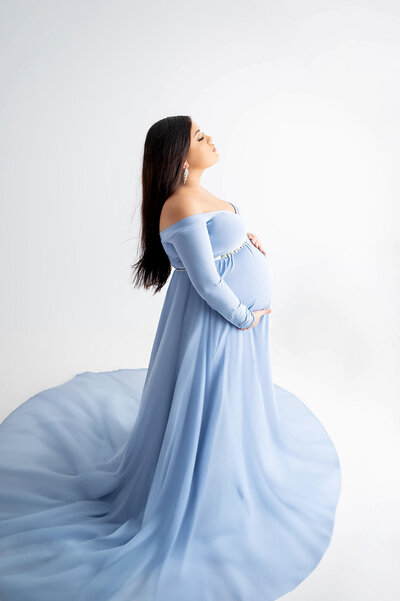 Woman facing to the side, gently cradles her pregnant belly as she closes her eyes surrounded by a soft glow. 