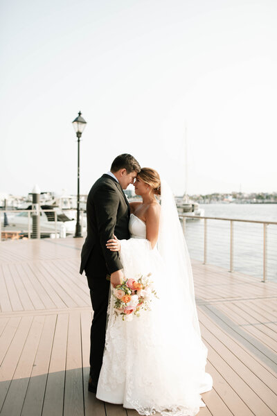 Couple in wedding attire standing forehead to forehead on NJ dock