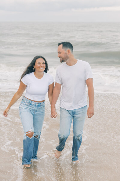 Couple holding hands and walking on beach during sunrise engagement session