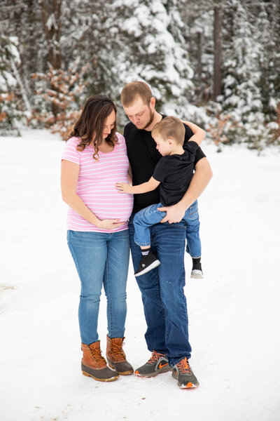 Family being photographed in snow, Mom is expecting | Maternity Photographer