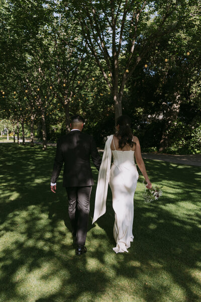 Bride and groom walking together under trees.