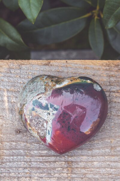 A moss agate heart crystal with green and burgundy colours.
