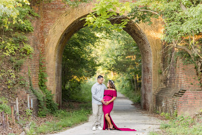 A mother-to-be in a red dress posing with her baby's father under a bridge in Lorton, Virginia.