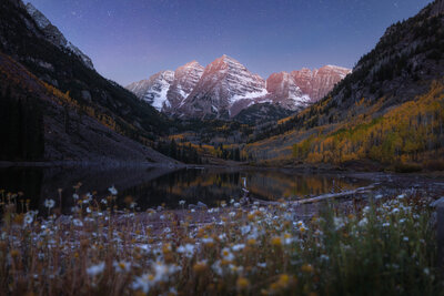 Stars shining over the Maroon Bells, at blue hour, during fall, with wildflowers in the foreground