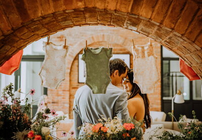 Couple celebrating at a baby shower with floral décor and baby clothes hanging on display, styled by Yours Truly, a wedding planner and designer in New Jersey.