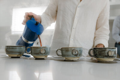 Coffee from blue moka pot being poured on ceramic cups