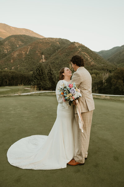 A photo of a bride and groom taken by Bailee Freeman Photography on a golf course. Green mountains behind the bridal couple. 