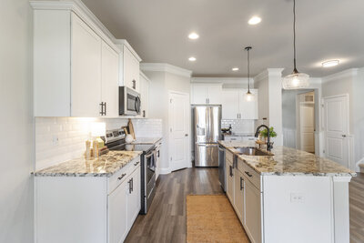 Bright kitchen featuring white cabinets, granite countertops, wood-look flooring, and a back door with large windows.