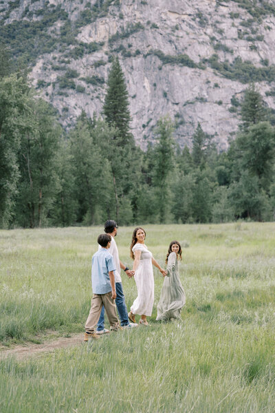 Mother and father walking with two kids in sunlit field | Fresno family photographer