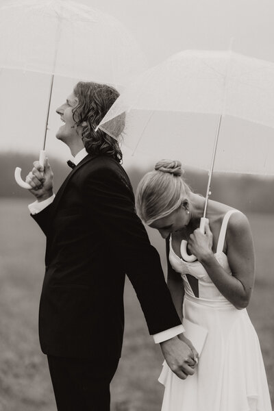 Bride and groom laughing under clear umbrellas on a rainy day in Alberta.
