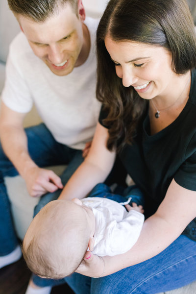 New mom and dad sit with their new baby on their laps and smile at him affectionately