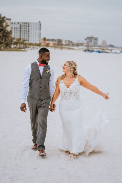 bride and groom holding hands while walking on the beach